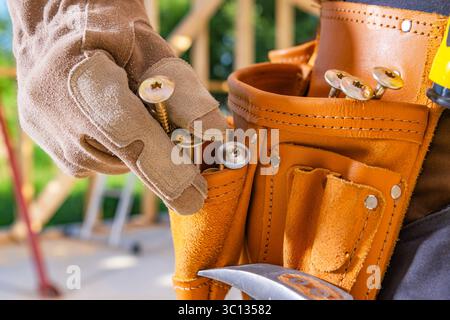 Ein Facharbeiter organisiert Schrauben in einem Werkzeuggürtel, während er auf einer Baustelle arbeitet. Stockfoto