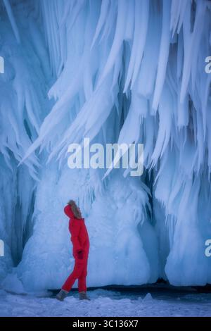 Baikal, Russland - 27. Januar 2022: Blick auf eine Einzelfigur in leuchtendem Rot, gegenüber den gefrorenen, geformten Eisformationen des Baikalsees, eine Studie in Kontrasten von Farbe und Textur. Stockfoto