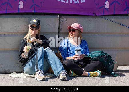 Junge Frauen, die auf dem Boden sitzen und beim World Village Festival im Stadtteil Suvilahti in Helsinki, Finnland, einen Drink trinken Stockfoto