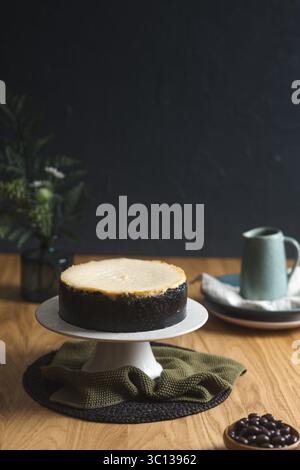 Hausgemachter Käsekuchen auf einer Schokoladen-Kekskruste, elegant präsentiert mit einem Keramikkkrug mit heißer Schokolade im Hintergrund. Stockfoto