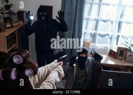 Frau, die maskierte Eindringlinge während eines Hauseinbruchs konfrontiert Stockfoto