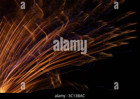 Vor dem schwarzen Hintergrund sieht die Nahaufnahme des orangen Feuerwerks aus wie die Schwanzfedern eines Pfaus. Es gibt Wärme und Energie im Bild. Stockfoto