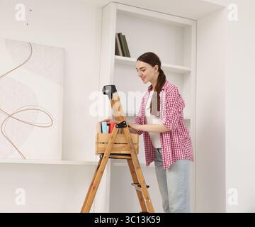 Frau, die zu Hause Bücher in Regale legt, indem sie Leiter benutzt Stockfoto