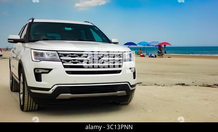 Nahaufnahme eines weißen Ford Explorer SUV, der an einem Strand mit weit entfernten Strandgängern parkt. Stockfoto