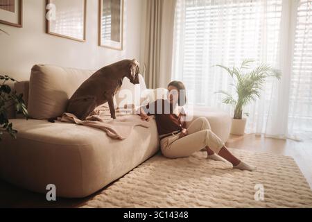 Gemütlicher Indoor-Moment Eine Frau genießt Eine schöne Zeit mit ihrem Hund, während sie auf einem Sofa sitzt Stockfoto