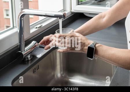 Frau, die ein Glas frisches Wasser aus einem modernen Küchenarmatur füllt Stockfoto