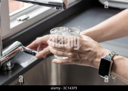 Frau füllt ein Glas frisches Wasser aus einem modernen Küchenarmatur Stockfoto