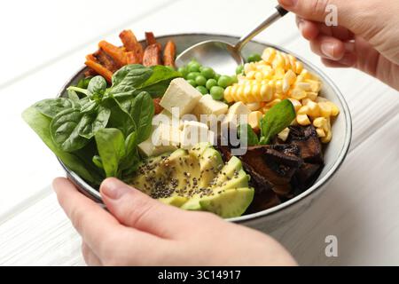 Gesundes vegetarisches Essen. Frau isst köstliche Buddha-Schüssel an weißem Holztisch, Nahaufnahme Stockfoto
