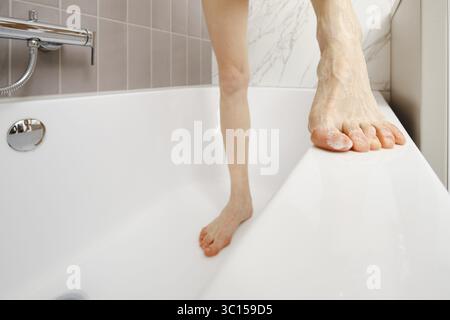 Eine Person balanciert am Rand einer Badewanne und zeigt einen Moment des täglichen Lebens. Das Badezimmer ist mit hellen Fliesen und einem eleganten Design ausgestattet, das die s betont Stockfoto