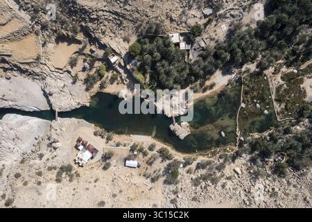 Aus der Vogelperspektive trifft man auf türkisfarbenes Wasser, felsige Klippen und üppiges Grün, was eine Oase der Ruhe schafft, Maskat, Maskat Governorate, Oman. Stockfoto