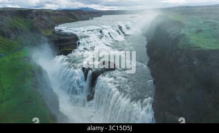 Mächtiges Wasser stürzt vom Gullfoss-Wasserfall und schafft einen nebeligen Schleier in der üppigen grünen Landschaft. Die dramatischen Klippen und das lebhafte Moos verstärken die ruhige und zugleich aufregende Atmosphäre. Stockfoto