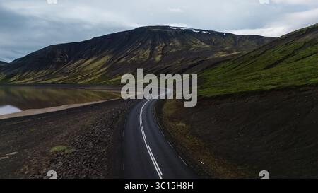 Eine gewundene Straße entlang der isländischen Küste bietet atemberaubende Ausblicke auf majestätische Berge und ruhiges Wasser. Stockfoto