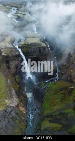 Ein atemberaubender Blick auf den Haifoss-Wasserfall, der von hohen Klippen in einen ruhigen Fluss unter Island stürzt Stockfoto