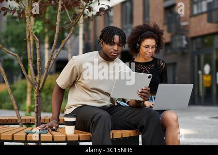 Ein junges afroamerikanisches Paar arbeitet gern draußen in der Stadt zusammen und sitzt auf einer Bank. Stockfoto