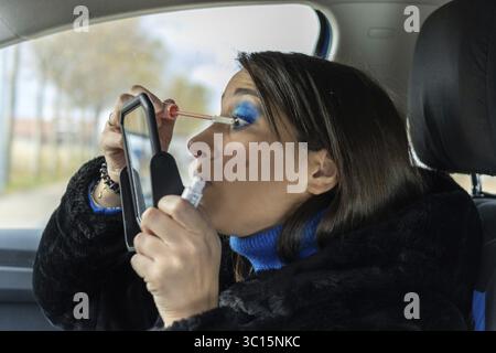 Schöne Frau, die Augen mit einem Spiegel im Auto schminkt Stockfoto