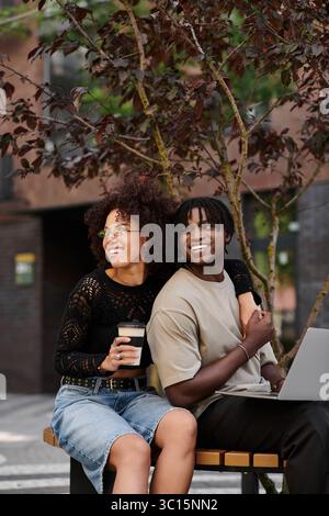 Das junge afroamerikanische Paar arbeitet gern fernab zusammen in einer lebhaften Stadtatmosphäre. Stockfoto