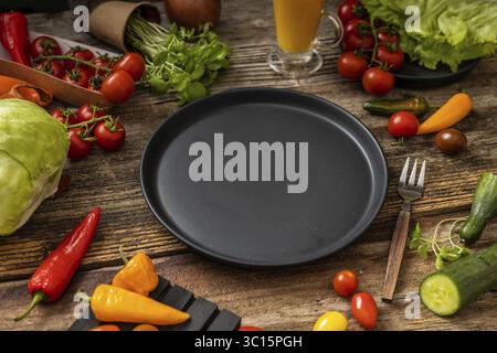 Schwarzer Teller auf Holztisch und -Gabel, Messer mit Holzgriff, viel Gemüse, Draufsicht Stockfoto