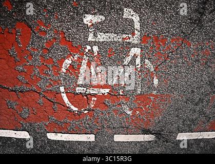 Ein abgenutztes Fahrradsymbol mit roten Farbspritzern auf Asphalt, das urbane Radwege zeigt, Reifenspuren Asphalt Streetview Stockfoto