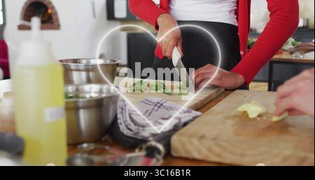 Frau in rotem Cardigan hacken und Partner, der Gemüse auf Brettern in der Küche mit Stahlschalen schneidet Stockfoto