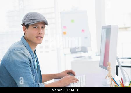 Mann, der an einem modernen Schreibtisch arbeitet und auf der Tastatur neben dem Computermonitor und der hölzernen Schaufensterpuppe tippt Stockfoto