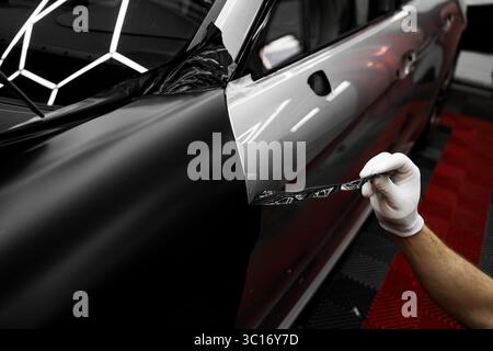 Die Anwendung „Auto Wrap“ ändert das Erscheinungsbild des Fahrzeugs. Vinyl-Verpackung Für Autos Mit Vollpaneel. Die großformatige Vinylfolie verwandelt das Außendesign des Fahrzeugs Stockfoto