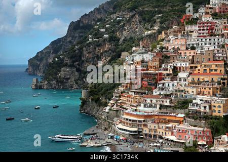 Weite Aufnahme: Bunte Häuser an den Klippen von Positano, die hinunter zum Fährhafen und dem Mittelmeer unten kaskadieren. Amalfiküste, Italien Stockfoto