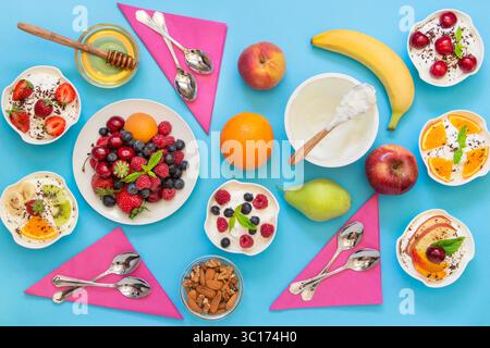 Eine lebendige Präsentation von frischem Obst, Joghurt, Nüssen und süßen Toppings, die künstlerisch auf einer blauen Tischdecke angeordnet sind, einladend und ideal für eine nahrhafte Mahlzeit oder einen Snack. Stockfoto