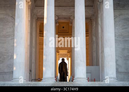 Jefferson Memorial Thomas Jefferson Statue Washington DC // WASHINGTON DC – die Bronzestatue von Thomas Jefferson ist durch die Säulen des nördlichen Portikus am Jefferson Memorial sichtbar, wobei goldenes Sonnenlicht die Hauptkammer kurz nach Sonnenaufgang beleuchtet. Die 5,8 Meter hohe Statue des Bildhauers Rudulph Evans zeigt den dritten US-Präsidenten und Urautor der Unabhängigkeitserklärung. Das 1943 fertiggestellte Jefferson Memorial wurde vom Architekten John Russell Pope im neoklassizistischen Stil mit einer runden Kolonnade aus ionischen Säulen entworfen. Die Gedenkstätte befindet sich auf dem Stockfoto