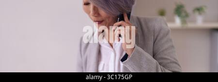 Fokussierte asiatische Profis kommunizieren effektiv über Smartphone. Geschäftsfrau nutzt Mobilgeräte für wichtige Gespräche an einem hellen Arbeitsplatz. Produkt Stockfoto