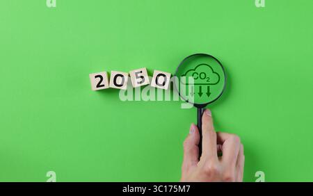 Konzept der CO2-Neutralität. Lupe mit CO2-Reduktionssymbol und dem Wort 2050 Jahr auf Holzblock. Zielvorgabe zur Verringerung der CO2-Emissionen, Stockfoto
