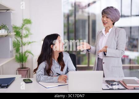 Zwei asiatische Geschäftsfrauen nehmen an einem produktiven Treffen in ihrem hellen Büro Teil. Sie diskutieren Strategien und fördern die berufliche Entwicklung und den Erfolg Stockfoto