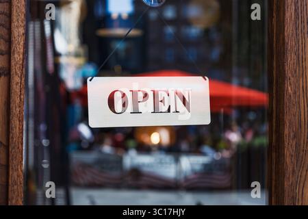 Open Sign on Storefront Glass mit verschwommenen Reflexen der City Street und im Outdoor Cafe Stockfoto