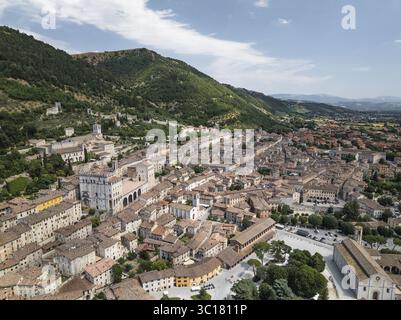 Blick aus der Vogelperspektive auf die Terrakotta-Dächer, die hinunter zur historischen Basilika Sant'Ubaldo, eingebettet an den grünen Hängen, Gubbio, Provinz Perugia, Italien. Stockfoto