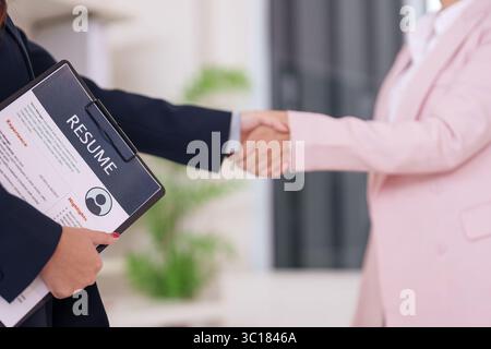 Zwei Geschäftsfrauen, die nach einem erfolgreichen Vorstellungsgespräch Hand schütteln. Der Bewerber hält während des Berufs-Einstellungsprozesses für eine neue Karriere einen Lebenslauf fest. Stockfoto