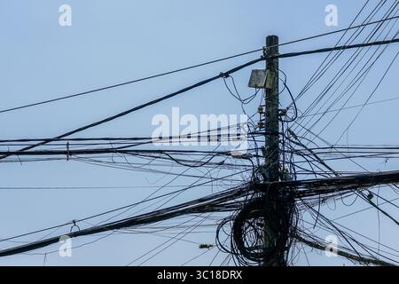 Ein dichtes Bündel von verworrenen Freileitungen und Kabeln hängt an einem Versorgungsmast, was die chaotische städtische Infrastruktur hervorhebt Stockfoto