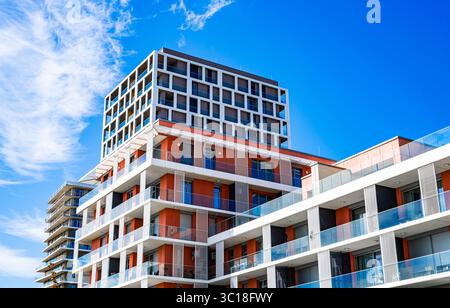 Modernes mehrstöckiges Wohngebäude mit lebhafter Fassade, großen Balkonen und malerischer Skyline unter klarem blauem Himmel Stockfoto
