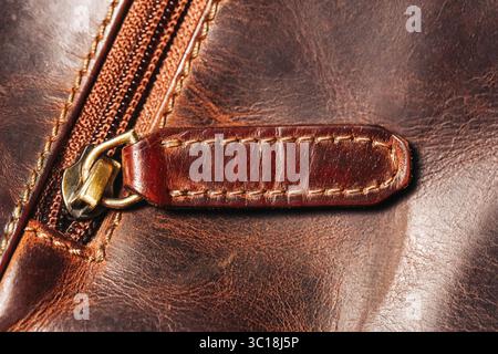 Lederreißverschluss. Nahaufnahme der braunen Tasche mit goldenem Metallabzieher. Hochwertige, genähte Textur. Makroansicht für Modeaccessoires. Stockfoto