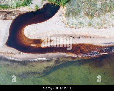 Drohnenansicht eines tanninreichen Flusses, der in Estland in die Ostsee fließt. Abstraktes Naturmuster und Hintergrund. Stockfoto