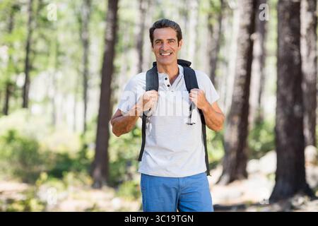 Mann, der durch dichte Kiefernwälder wandert, trägt schwarzen Wanderrucksack unter Sonnenlicht Stockfoto