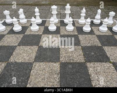 Freiluft-Schachspiel mit weißen Figuren auf Schwarz-weiß-Brett. Kopierraum Stockfoto