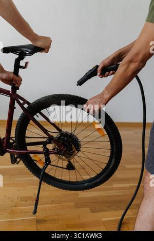 Vertikale Nahaufnahme zweier Mechaniker, die das Mountainbike-Rad mit einem Dampfreiniger reinigen, um eine gründliche Wartung und Hygiene zu gewährleisten Stockfoto