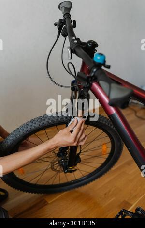 Vertikal geschnittene Aufnahme eines mechanischen männlichen Mannes, der die Vordergabel des Fahrrads mit einem weißen Tuch reinigt, um eine reibungslose Leistung zu gewährleisten und das Motorrad zu erhalten Stockfoto