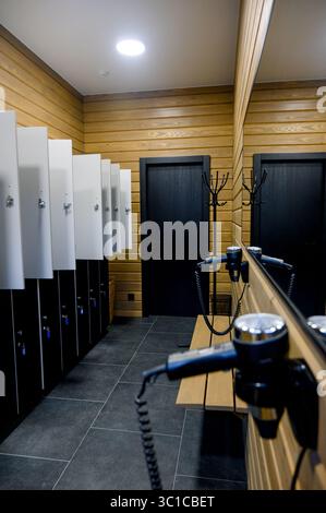 Moderne Umkleideräume mit Holzverkleidungen und Schließfächern. Umkleideraum mit Schließfächern, Spiegeln und Haartrockner Stockfoto