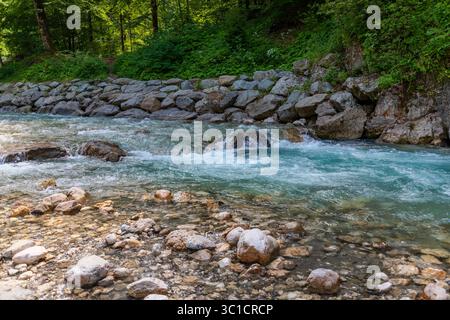 Klarer Alpenbach mit türkisfarbenem Wasser, das über glatte Steine in der Nähe eines Waldweges in Garmisch-Partenkirchen, Bayern, fließt. Eine friedliche Naturszene Stockfoto