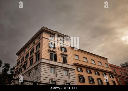 Schräger Blick auf einen römischen Wohnblock aus dem späten 19. Jahrhundert mit cremefarbenen und ockerfarbenen Fassaden, Fensterläden und dekorativen Gesimsen Stockfoto