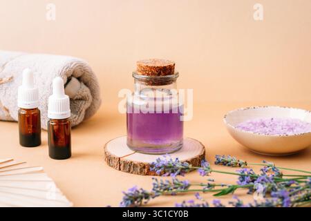 Lavendelöl, Badesalz und Handtuch für Spa-Behandlung auf beigem Hintergrund. Aromatherapiekonzept. Stockfoto