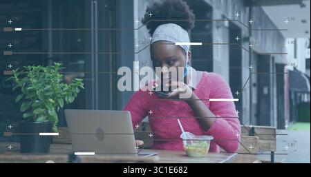 Mit Laptop-Frau in rosa Pullover, die in das Smartphone auf der Terrasse des Cafés mit Salatbehälter spricht Stockfoto