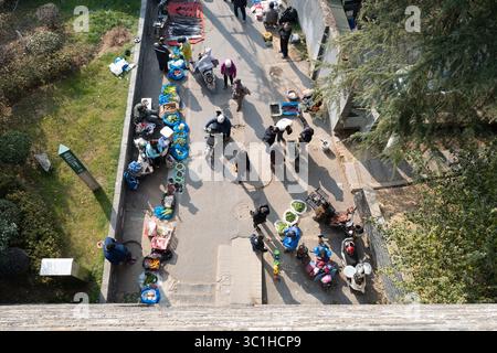 Ein Blick von oben zeigt einen lebhaften Markt im Freien in Nanjing, wo zahlreiche Straßenverkäufer und Fußgänger auf einem schmalen Pfad geschäftig sind. Stockfoto