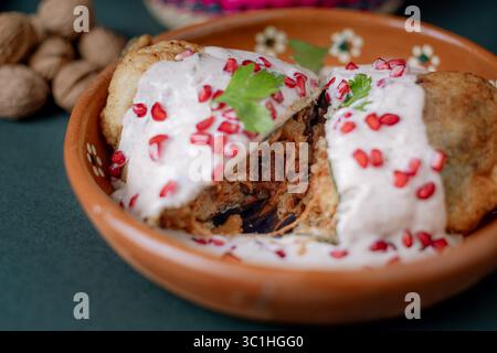 chile en nogada in Scheiben geschnitten, um seine traditionelle Fleisch- und Fruchtfüllung zu enthüllen, bedeckt mit cremiger Walnusssauce und Granatapfel. Stockfoto