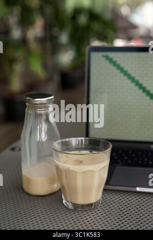Eiskaffee in einem Glas mit einem Laptop im Hintergrund. Fernarbeit oder freiberufliches Konzept in einem Café im Freien. Moderner Lifestyle mit Technologie. Stockfoto